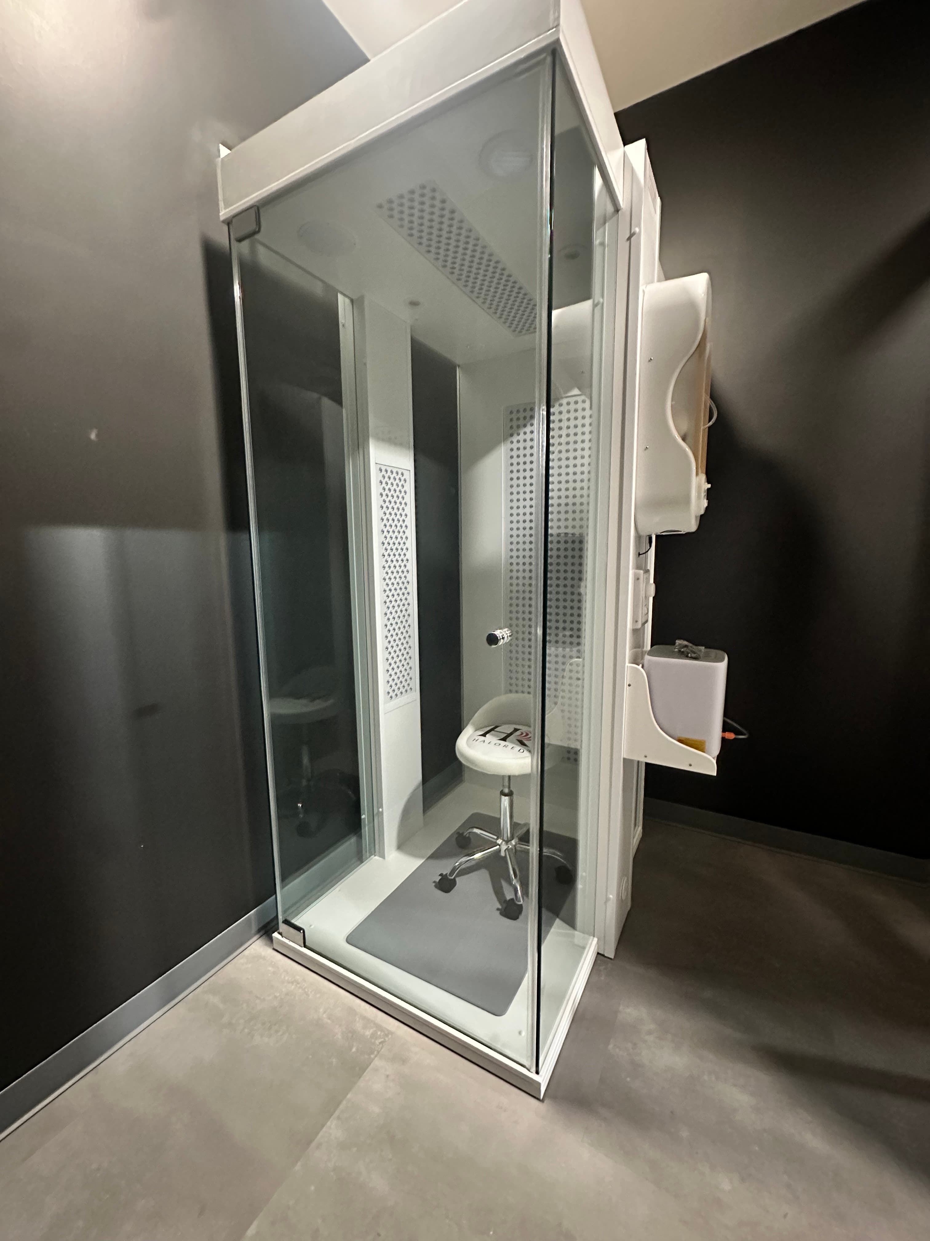 The HaloRed O₂ booth with the lights off, showing the glass enclosure, seat, and halogenerator