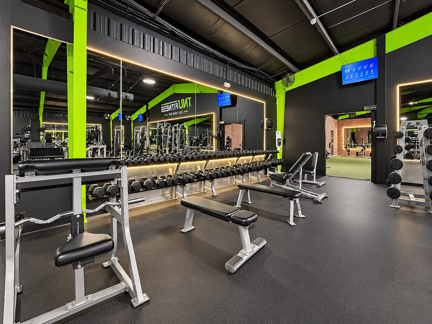 Dumbbells and benches lit by warm strip lighting at TNU Fitness